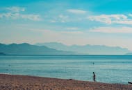 在晴朗的蓝天下，宁静的海滩可以欣赏到远处的山景，是放松的理想选择