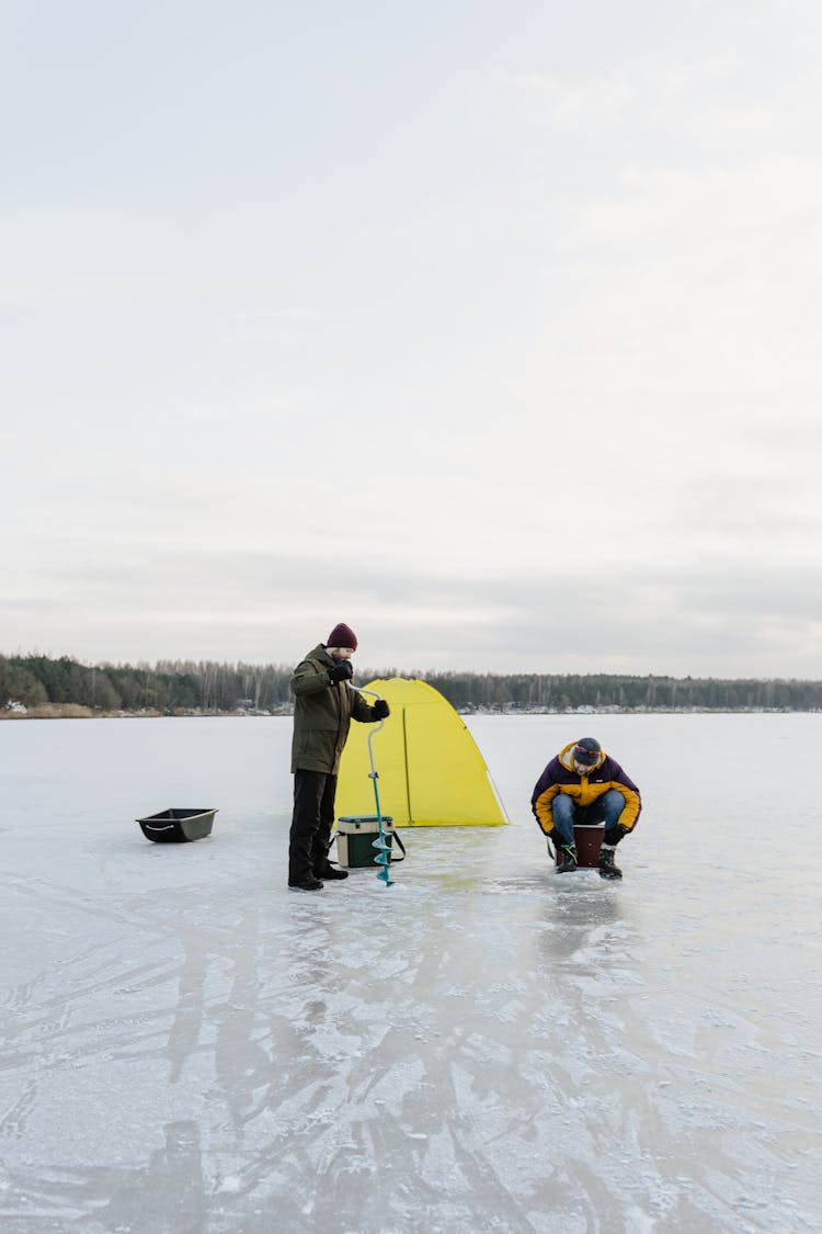 A Person Drilling A Hole On A Frozen Lake 