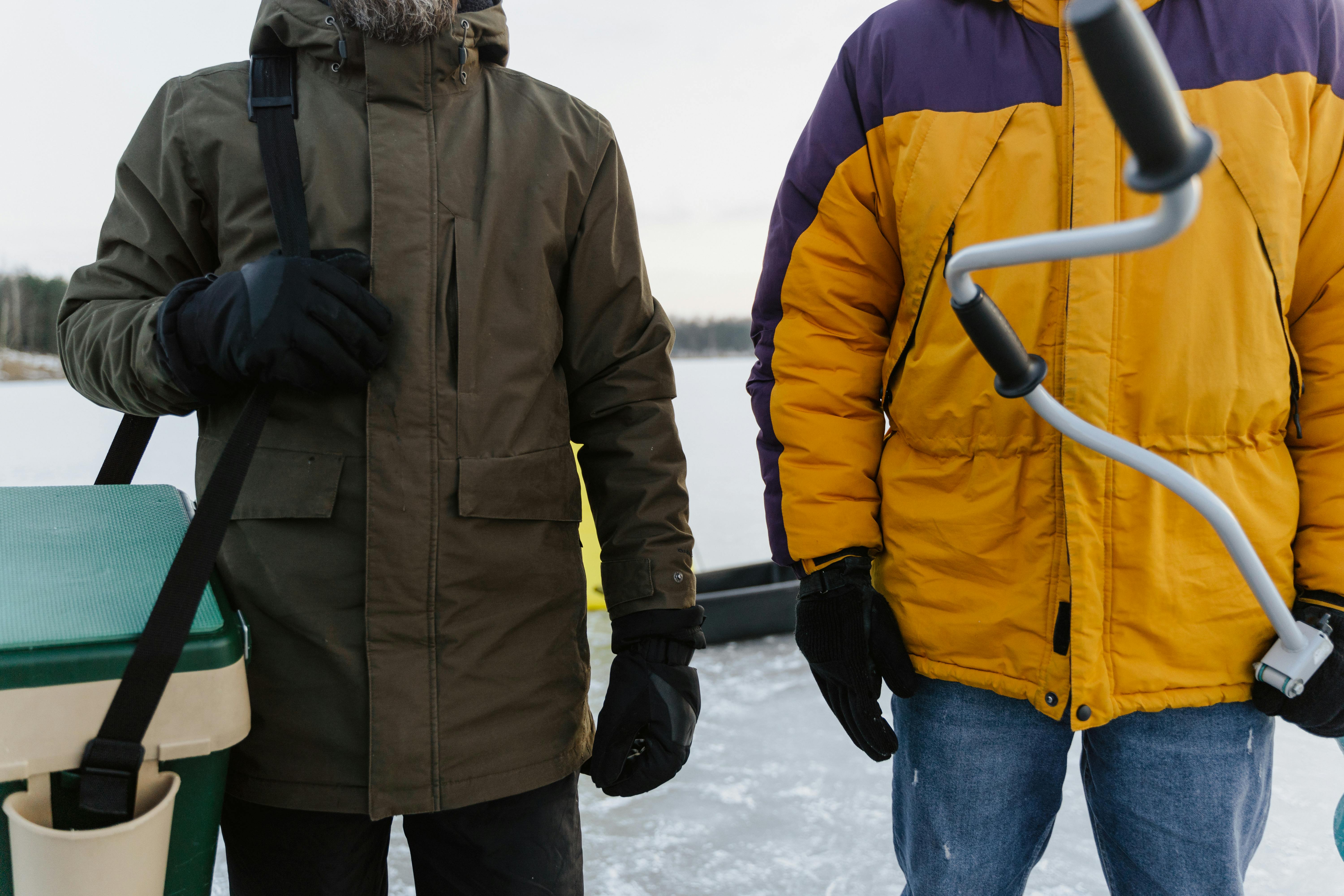 Close-up of two people preparing for ice fishing in winter, wearing jackets.