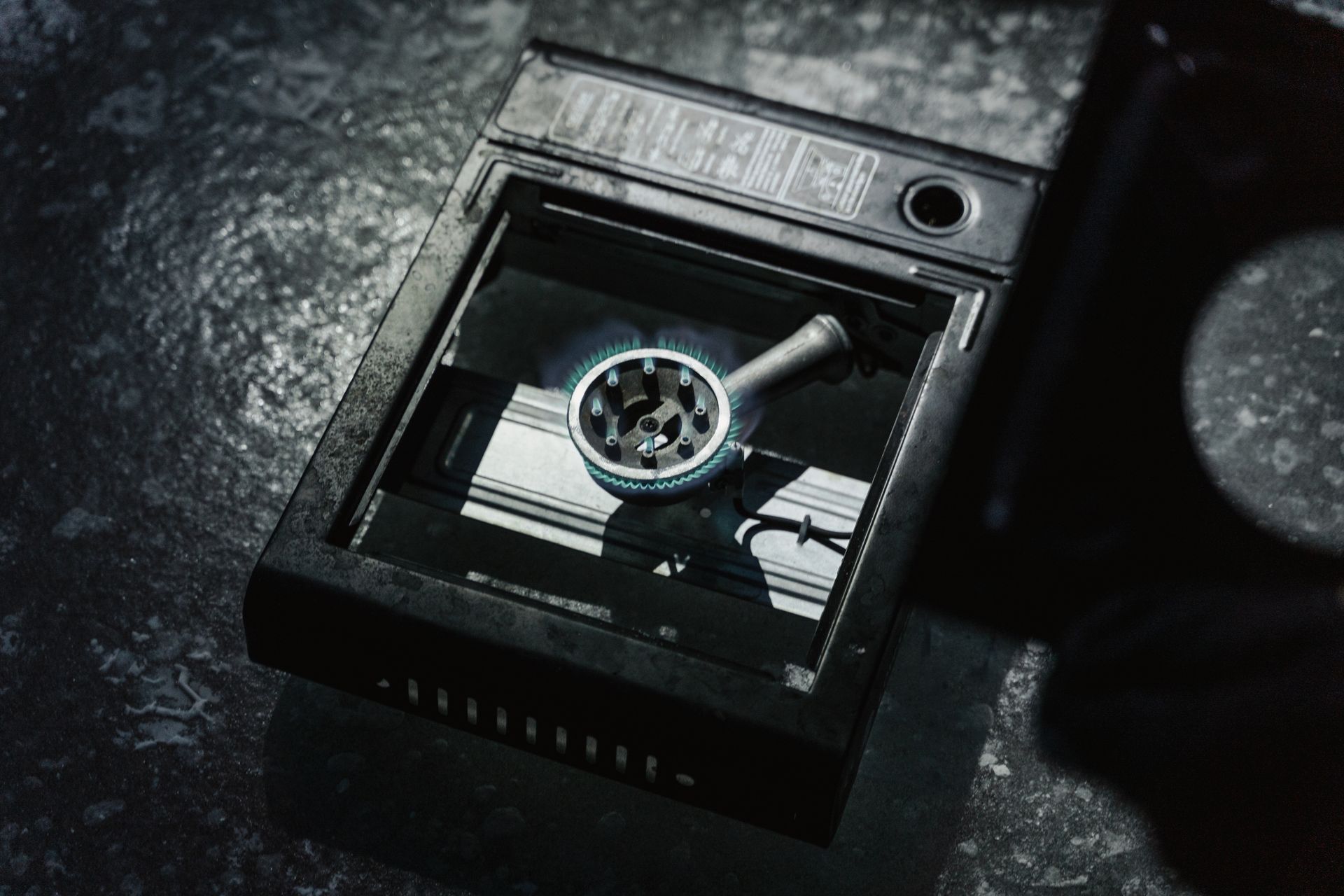 Detailed view of a portable stove with a lit blue flame on a textured surface.