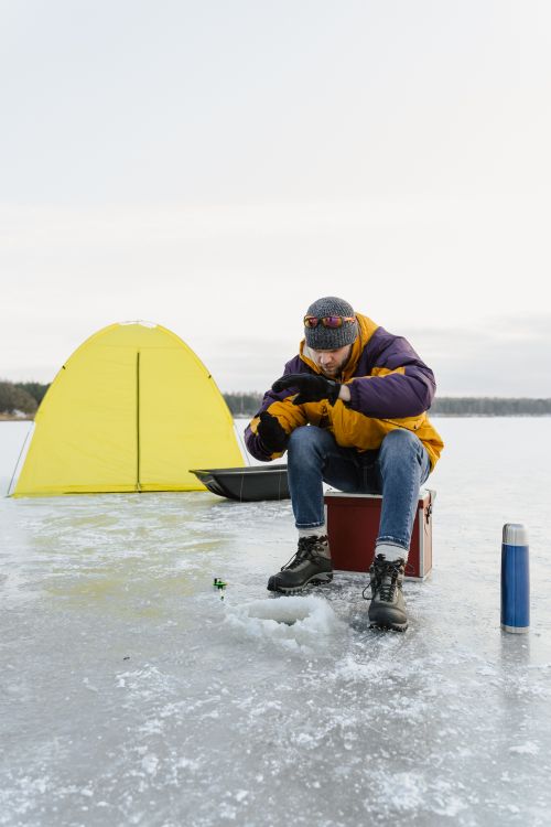 Free A man enjoys ice fishing on a frozen lake beside a yellow tent on a winter day. Stock Photo