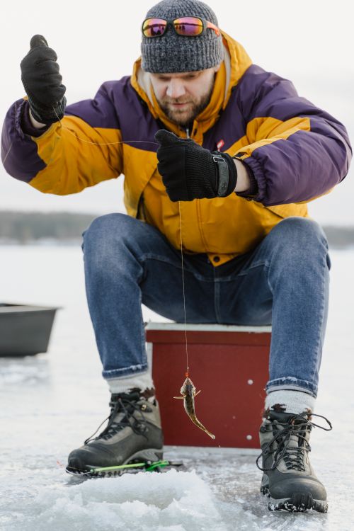 Free Man enjoying ice fishing on a frozen lake. Wearing winter clothing and holding a small fish. Stock Photo
