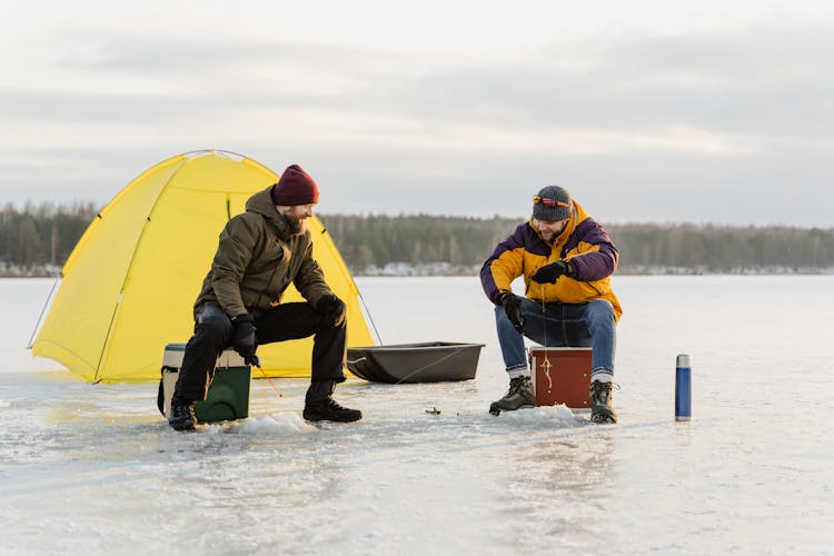 Men Sitting On Coolers Near A Tent Fishing On Ice