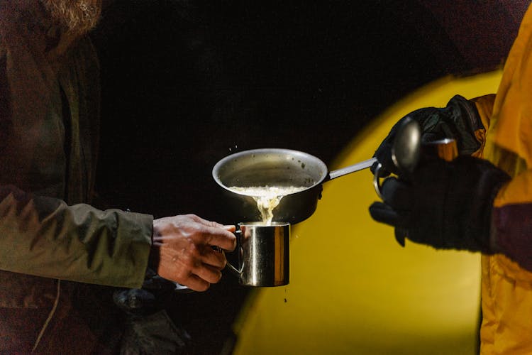 A Person Pouring Food In Silver Cup