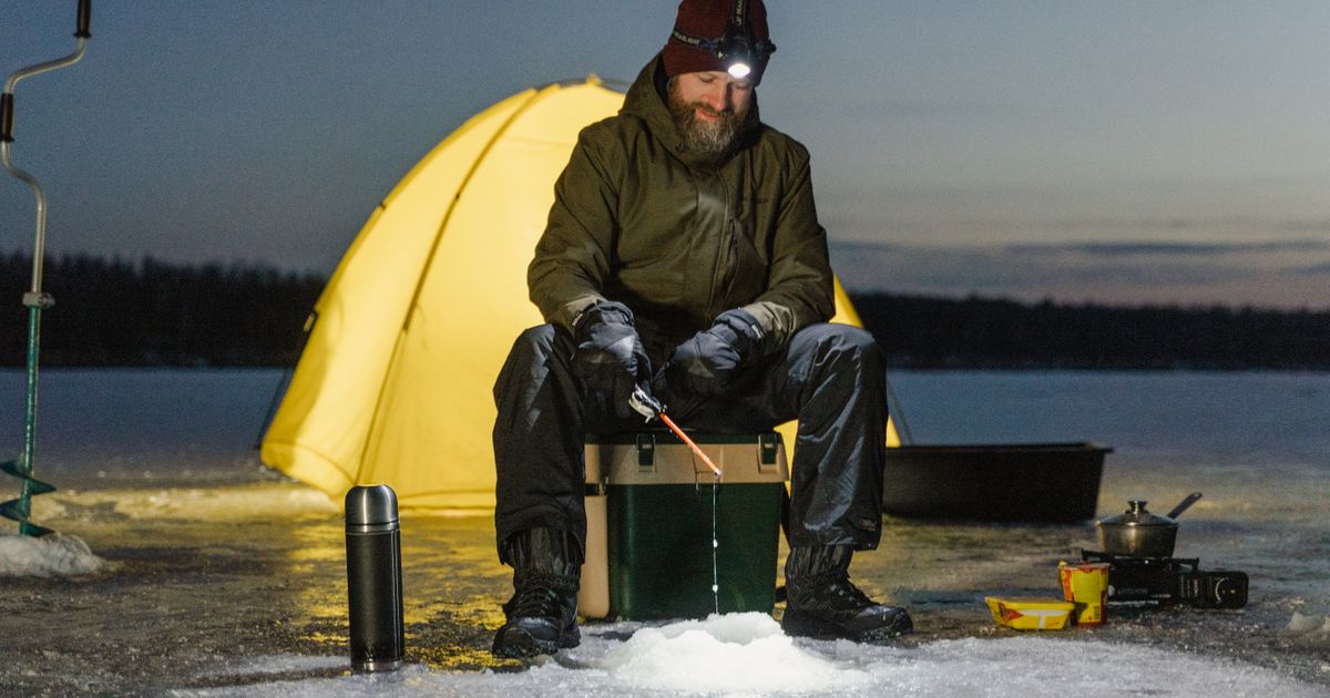 A man wearing a headlamp beside a yellow tent at dusk