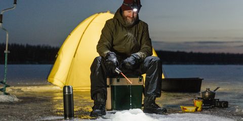 A man wearing a headlamp beside a yellow tent at dusk