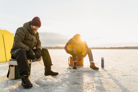 Two friends enjoy ice fishing on a frozen lake at sunrise, embracing the winter chill and outdoor adventure.