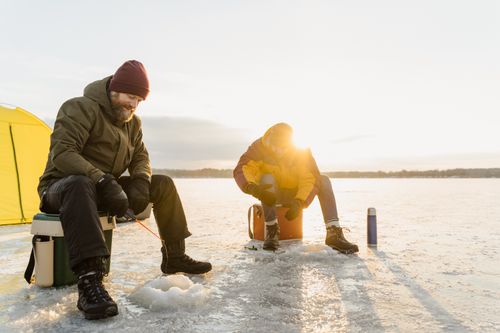 Free Two friends enjoy ice fishing on a frozen lake at sunrise, embracing the winter chill and outdoor adventure. Stock Photo