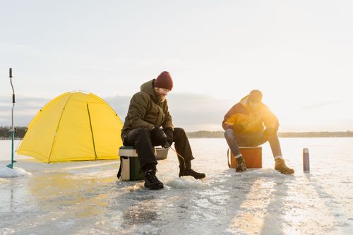 Free Two men enjoying ice fishing on a frozen lake beside a bright yellow tent. Stock Photo