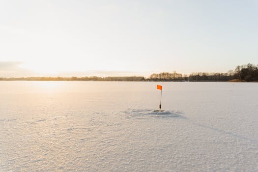 A tranquil winter lake with a solitary ice fishing flag marker during sunset.