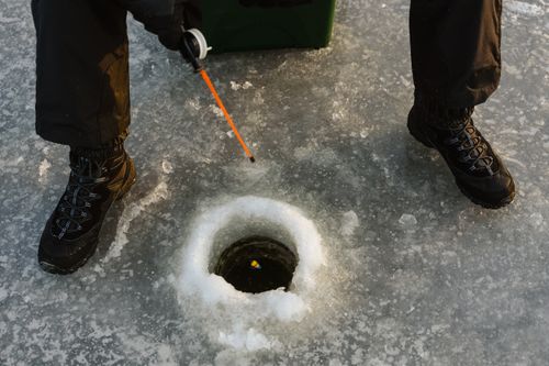 Free Person ice fishing on frozen lake surface with fishing rod and winter boots. Stock Photo