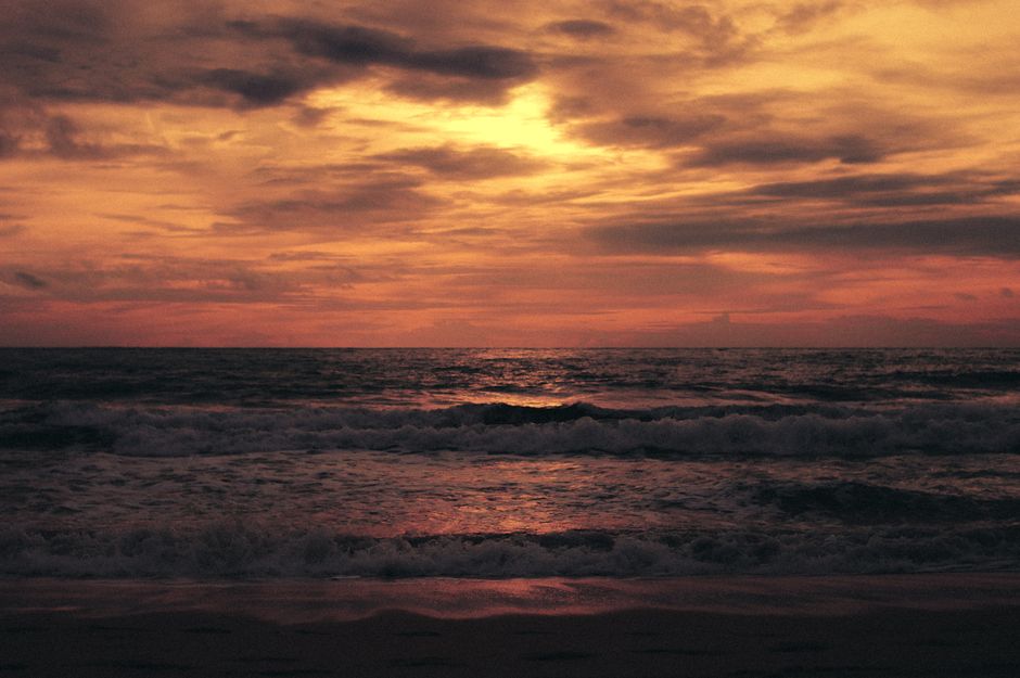 Picturesque view of waving endless sea washing sandy coast under cloudy sky at sundown