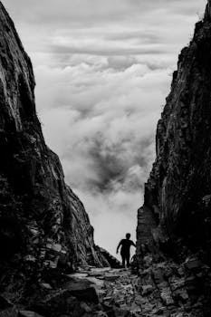 云层弥漫的天空下，一个登山者的剪影在崎岖的悬崖上穿行