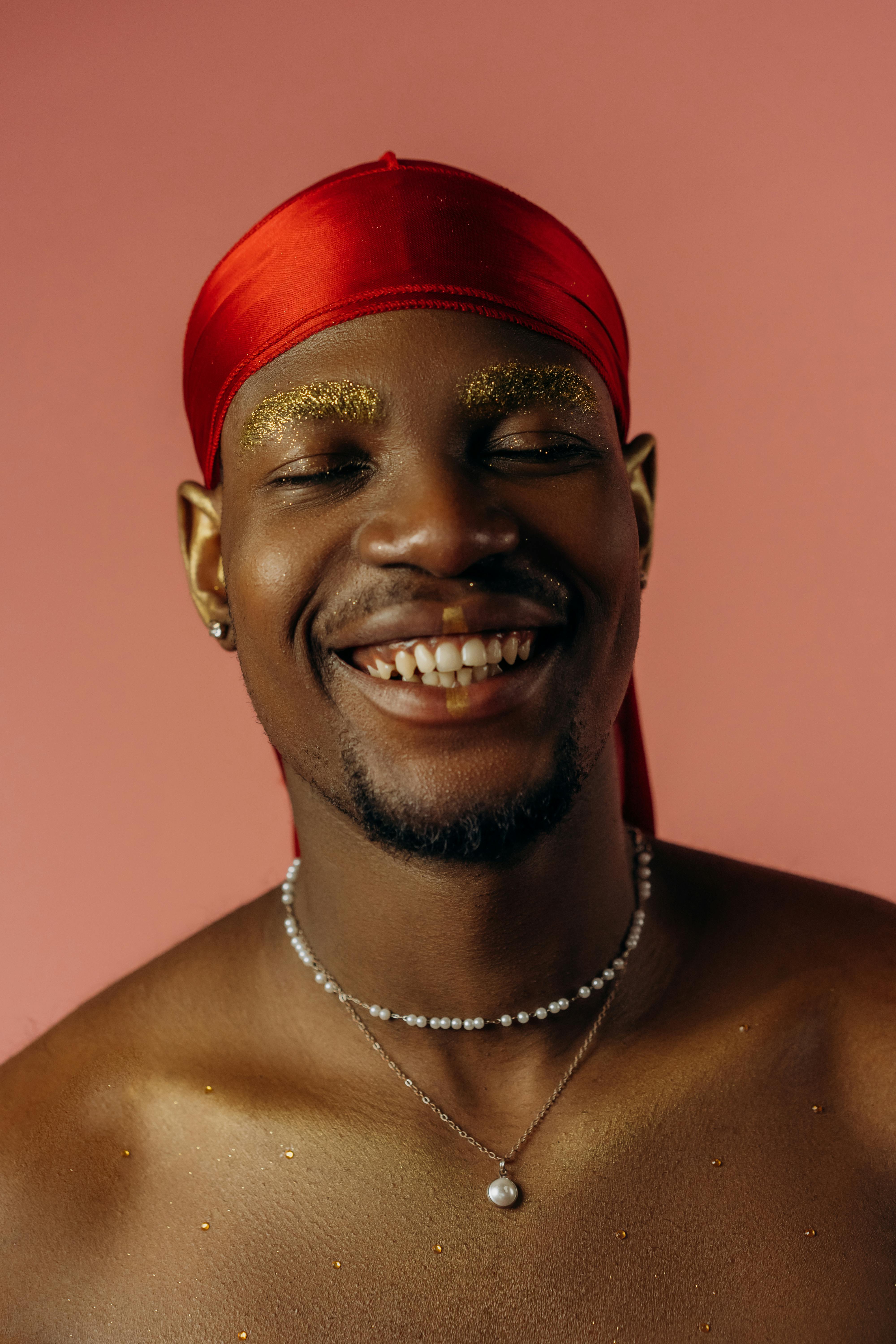 Close-up portrait of a smiling man wearing a red durag, with glitter details, in a studio setting.