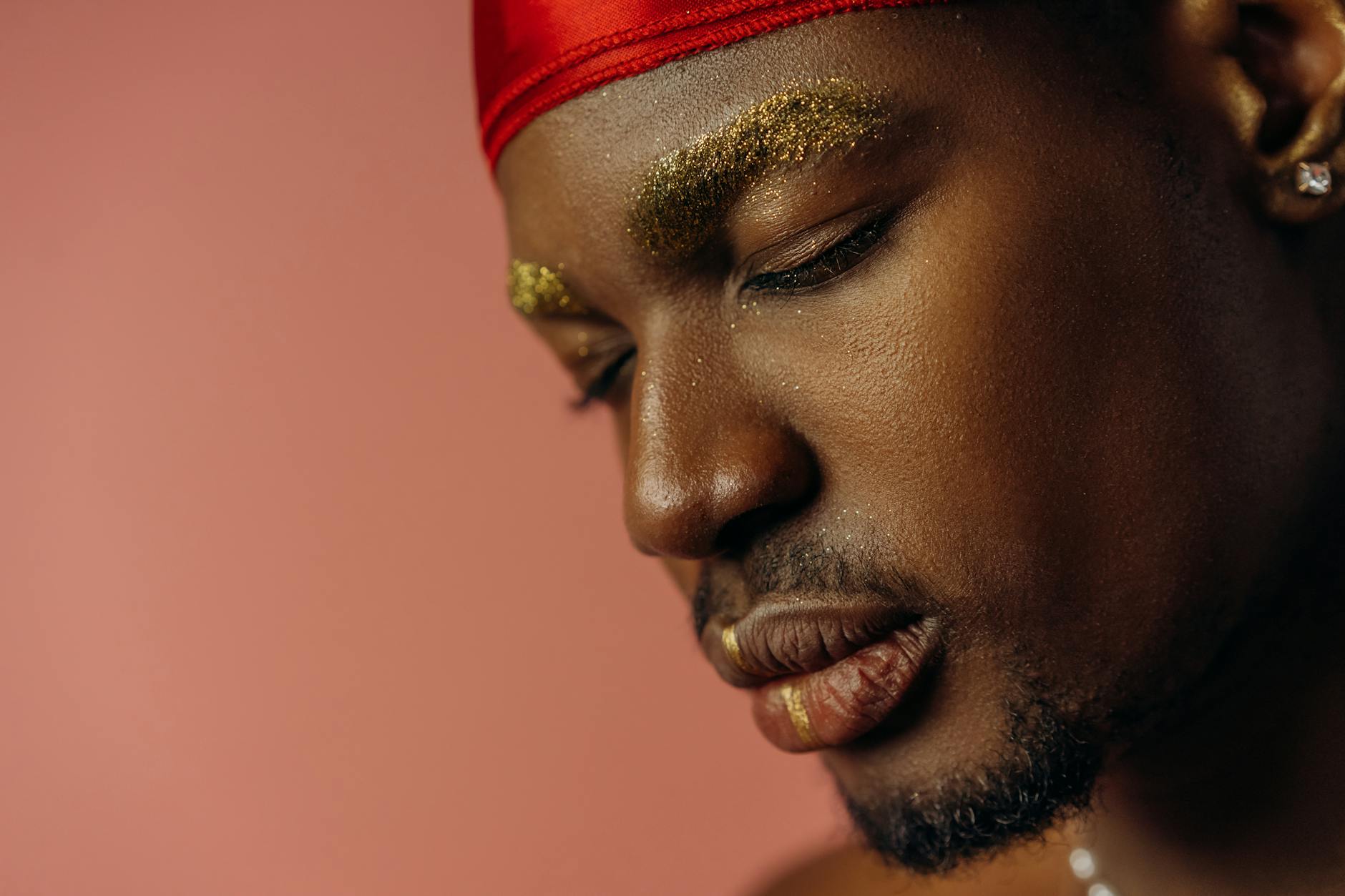 Artistic portrait of a man with golden eyebrow makeup against a soft background.
