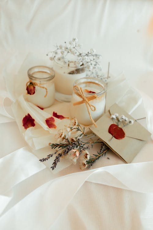 From above of flowers and twigs placed on white textile near scented candles and old fashioned envelope with wax stamp