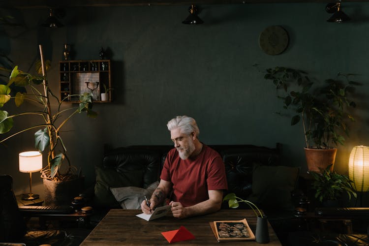 An Elderly Man Writing On A Card