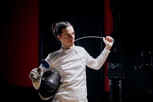 A fencer in full gear practicing indoors, holding a foil sword.
