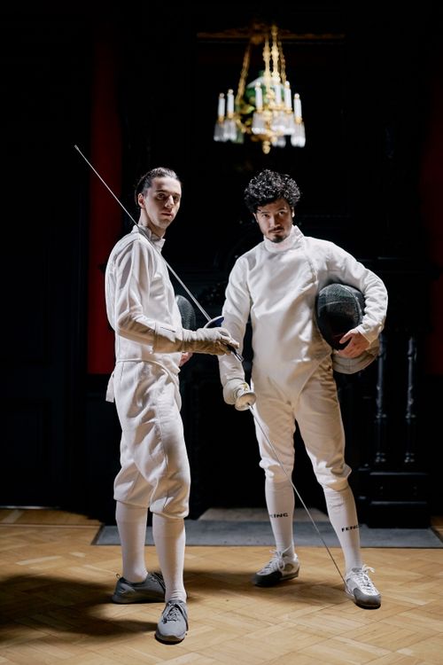 Free Two male fencers in full gear pose with swords indoors, ready for combat. Stock Photo