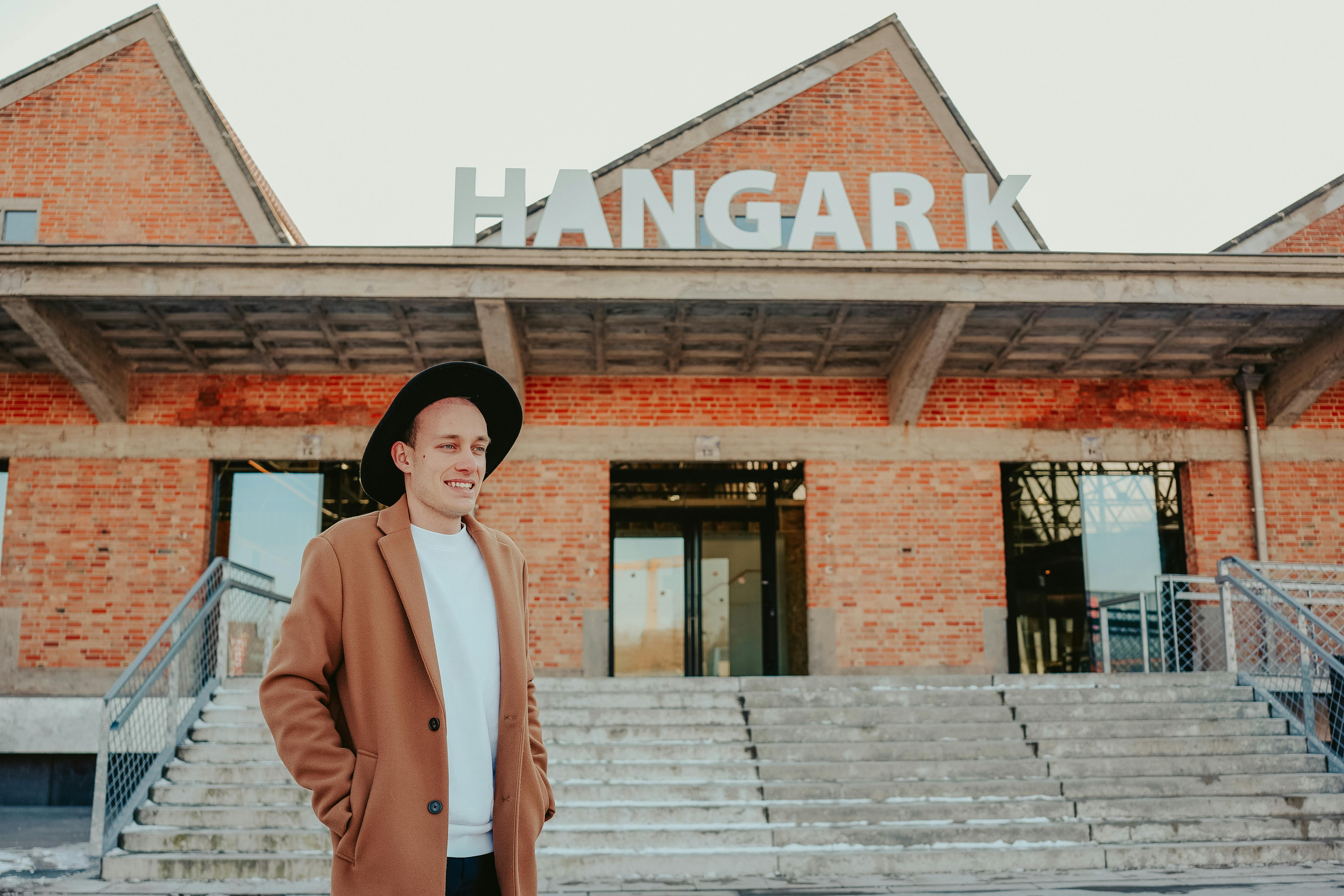 A stylish man with a hat in front of the iconic Hangar K building.