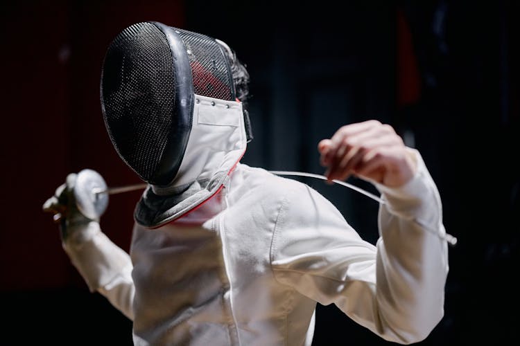 Person Wearing A Fencing Mask Holding A Sword Over His Shoulders