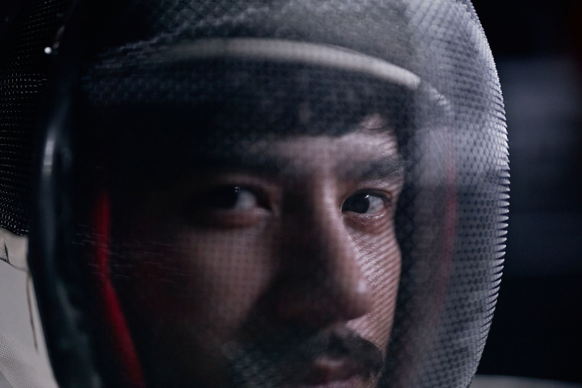 Intense close-up of a fencer wearing a protective mask, focusing on the eyes.