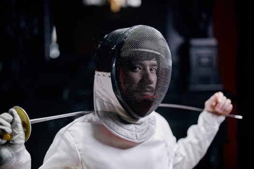 Fencer in full gear holding a foil, captured indoors with a focused expression.
