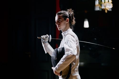 Free A determined male fencer in professional gear holds an epee indoors with dramatic lighting. Stock Photo