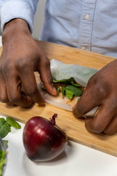 Close-up of hands wrapping fresh spring rolls with vegetables on a cutting board.