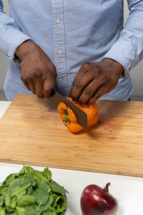 Man in Blue Shirt Holding Cutting a Bell Pepper