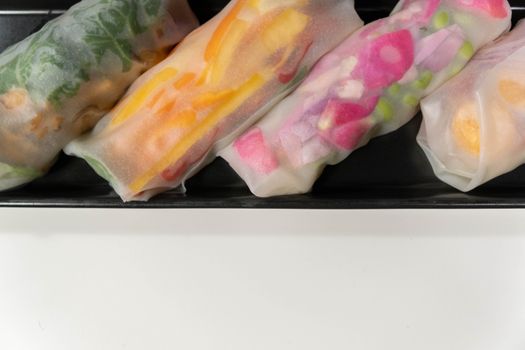 Colorful fresh spring rolls with vegetables on a minimalist white background, offering copy space.