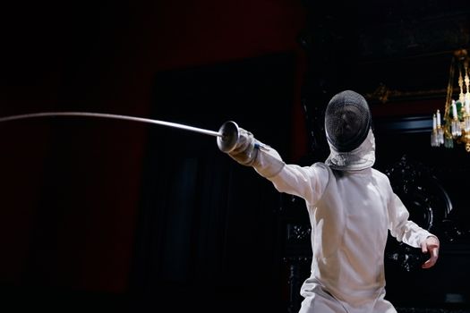 Fencer in full gear performing a sword thrust indoors, showcasing agility and technique.