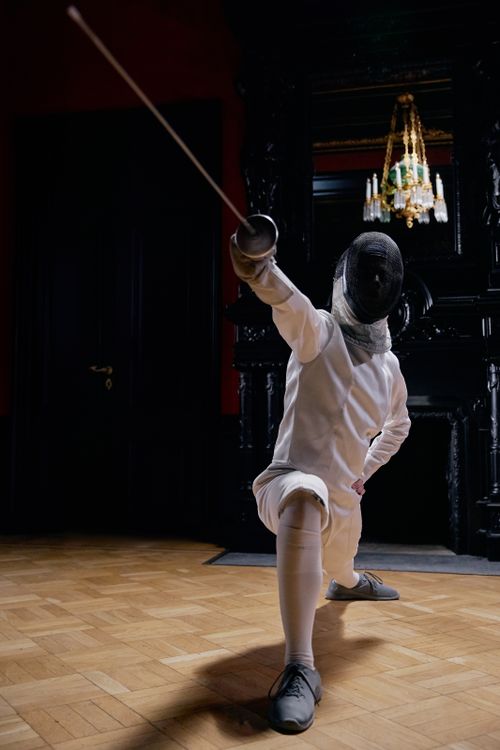 Free A fencer in full gear striking a dynamic pose with a sword indoors, showcasing focus and athleticism. Stock Photo