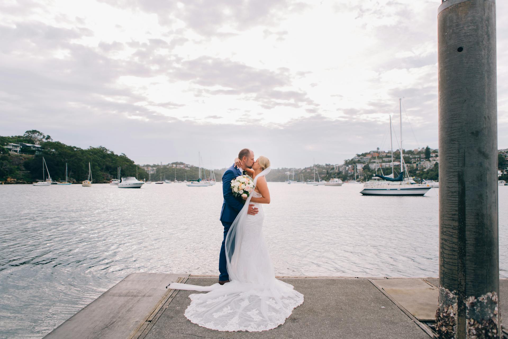 Bride and groom share a romantic kiss on a dock in Mosman, NSW with boats in the background.