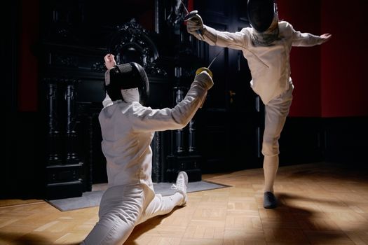 Two fencers in protective gear engaged in a dynamic duel in an elegant indoor setting.
