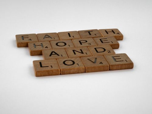 Free Wooden Scrabble tiles arranged to spell Faith, Hope, and Love against a white background. Stock Photo