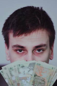 A young man holding and partially hiding behind Romanian lei banknotes, captured indoors.