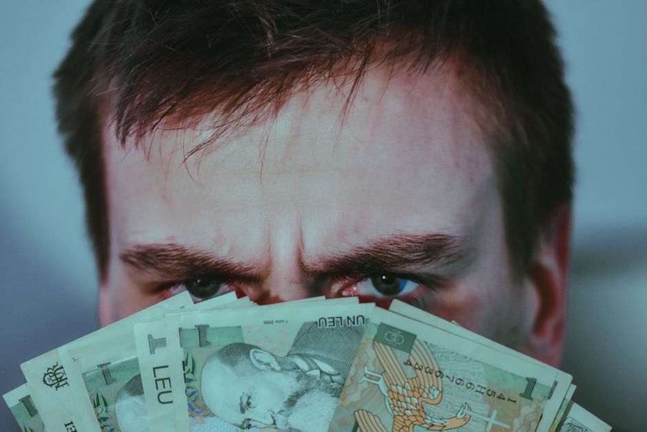 Crop unrecognizable frown man with dark hair covering face with stack of Romanian leu banknotes and looking at camera Crop unrecognizable frown man with dark hair covering face with stack of Romanian leu banknotes and looking at camera