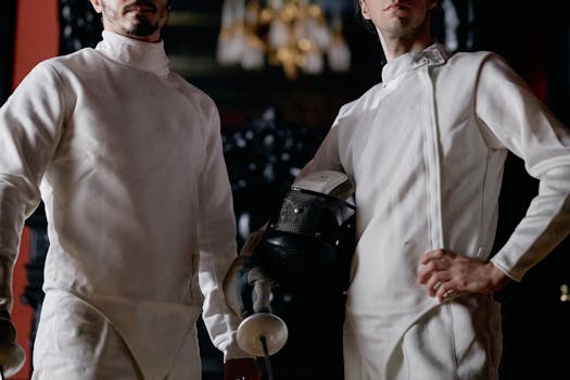 Two fencers in full gear pose confidently indoors, showcasing their equipment.