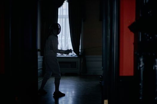 A fencer in silhouette practicing in a dimly lit room, showcasing athletic grace.