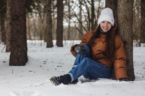 Woman Sitting on Snow Covered Ground Beside Tree