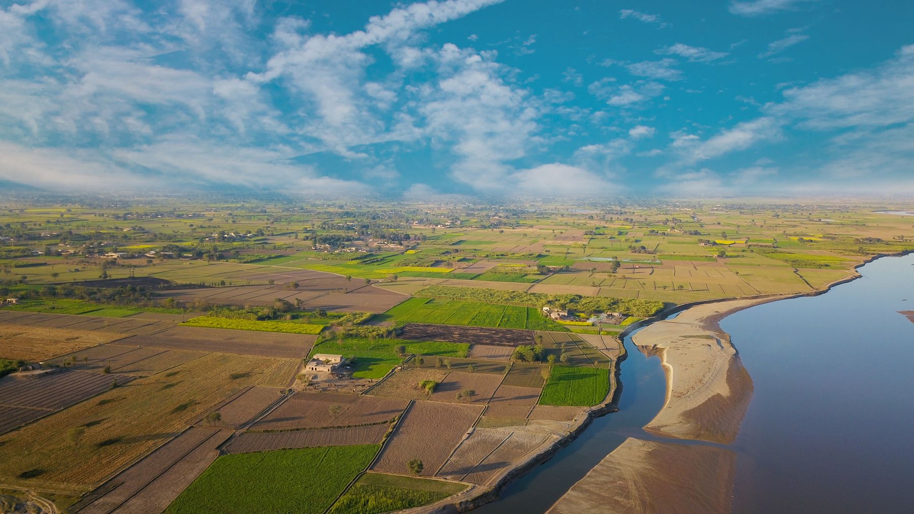 Breathtaking aerial view of vibrant fields and a winding river in Punjab, Pakistan.
