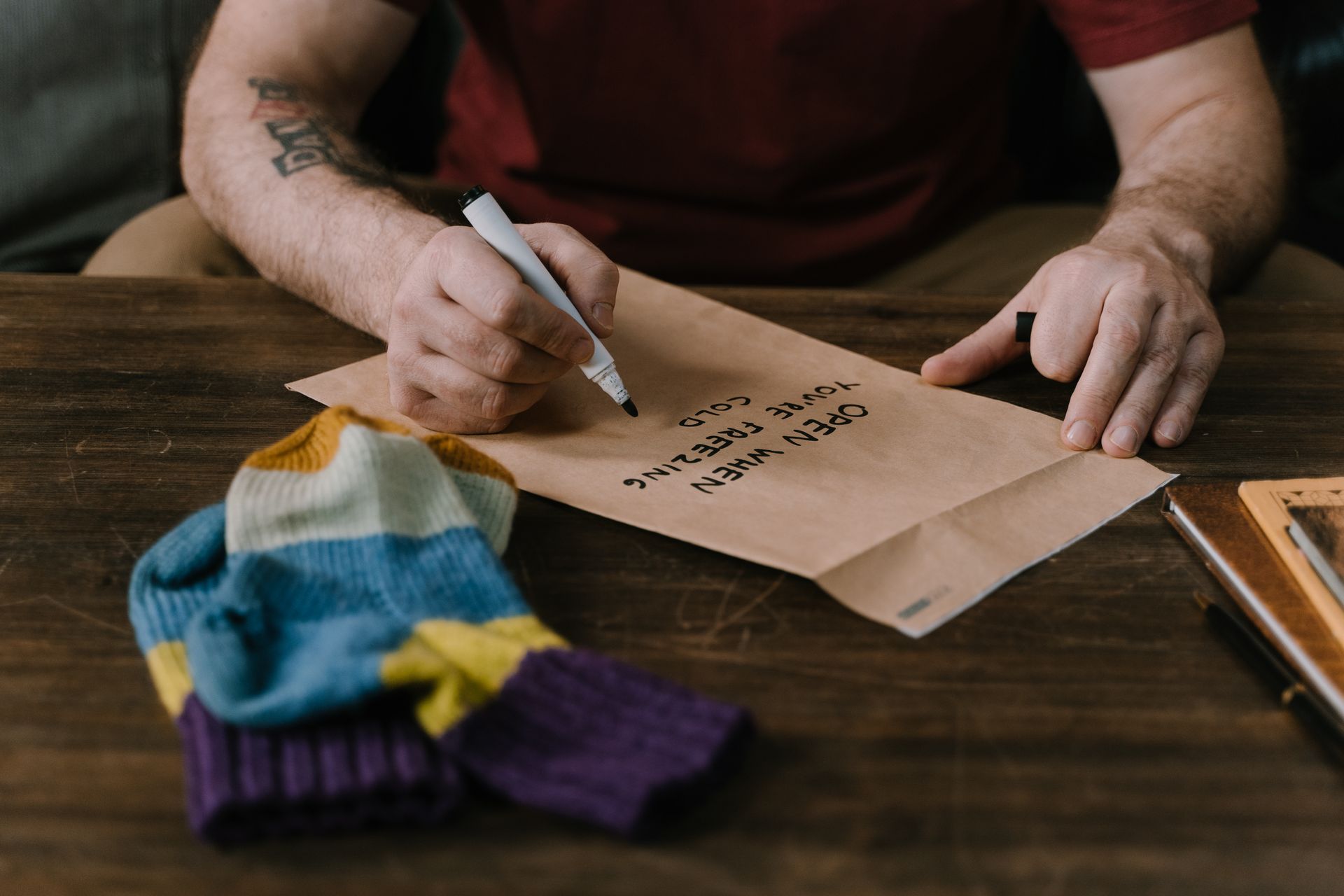Close-up of hands writing a message on an envelope with a colorful sweater beside it.