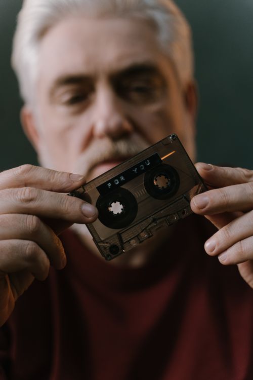 Free A senior adult holds a vintage cassette tape with focus on the tape in a moody setting. Stock Photo
