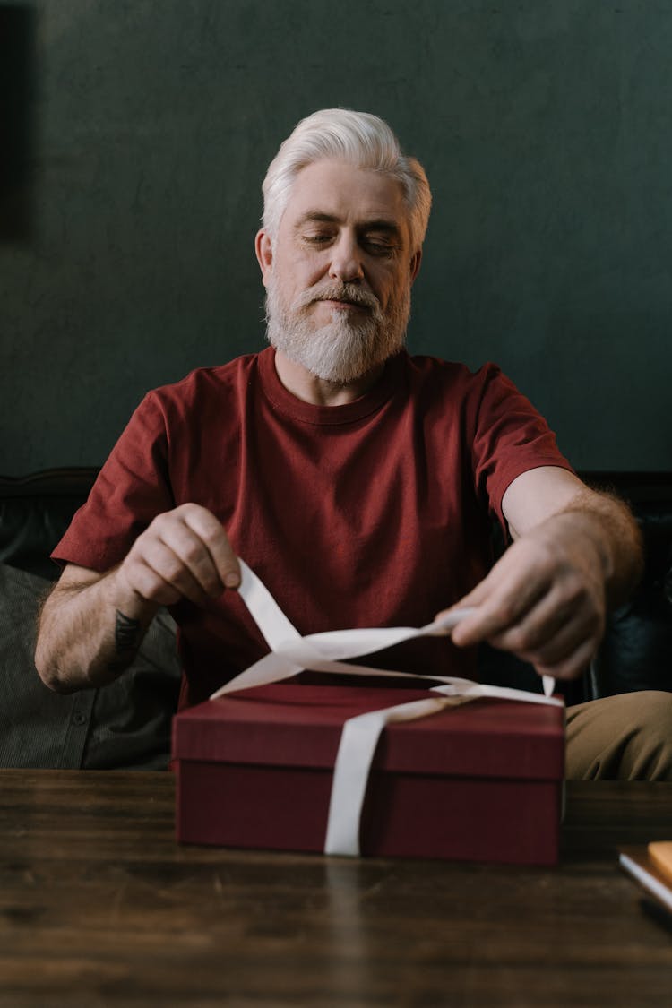 An Elderly Man Tying Ribbon On A Gift Box