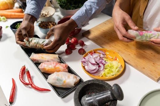 Two people preparing fresh vegetable spring rolls on a kitchen counter with various ingredients.