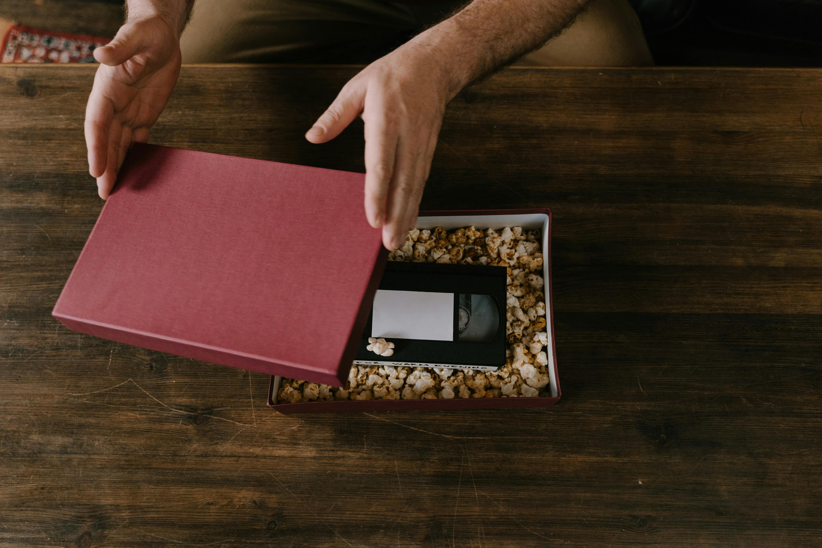 a person opening a box with popcorn and a videotape