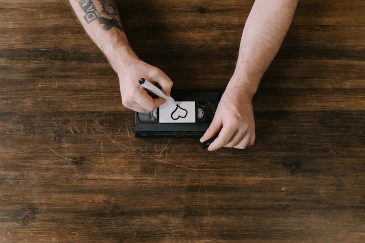 A Person Writing A Heart Icon On The Videotape Label