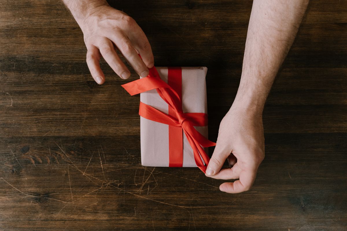 Hands tying a red ribbon on a gift box