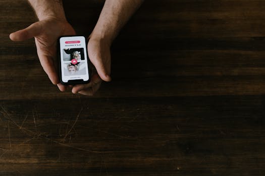 Close-up of hands holding a smartphone with a social media app open on a wooden table.